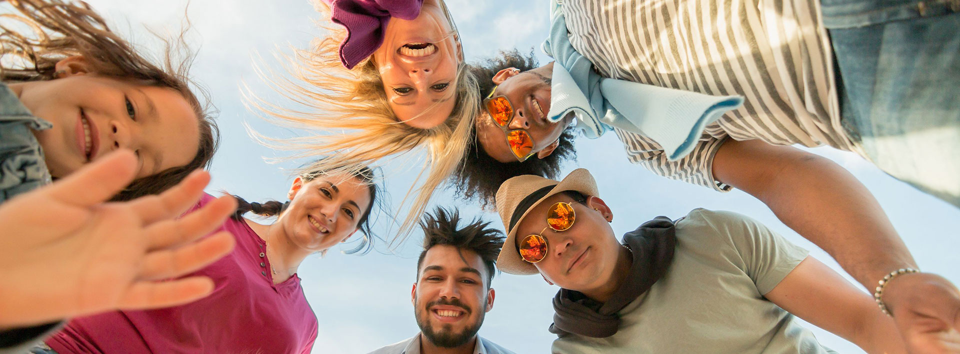 Camera looking up at a circle of three men, two women, and a girl. Everyone is smiling.